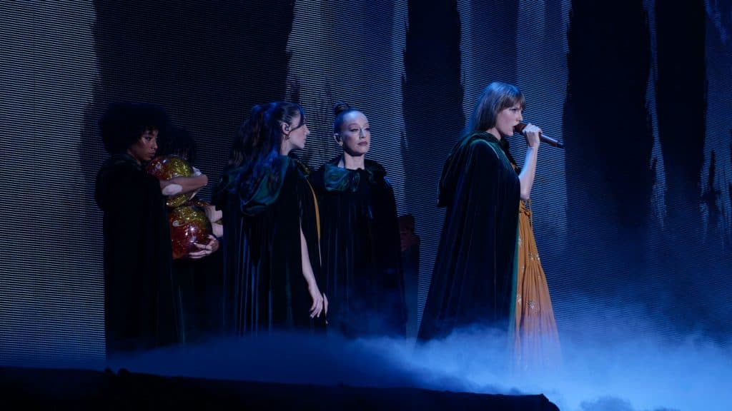 Taylor Swift wearing a black cape and performing onstage during her Eras Tour