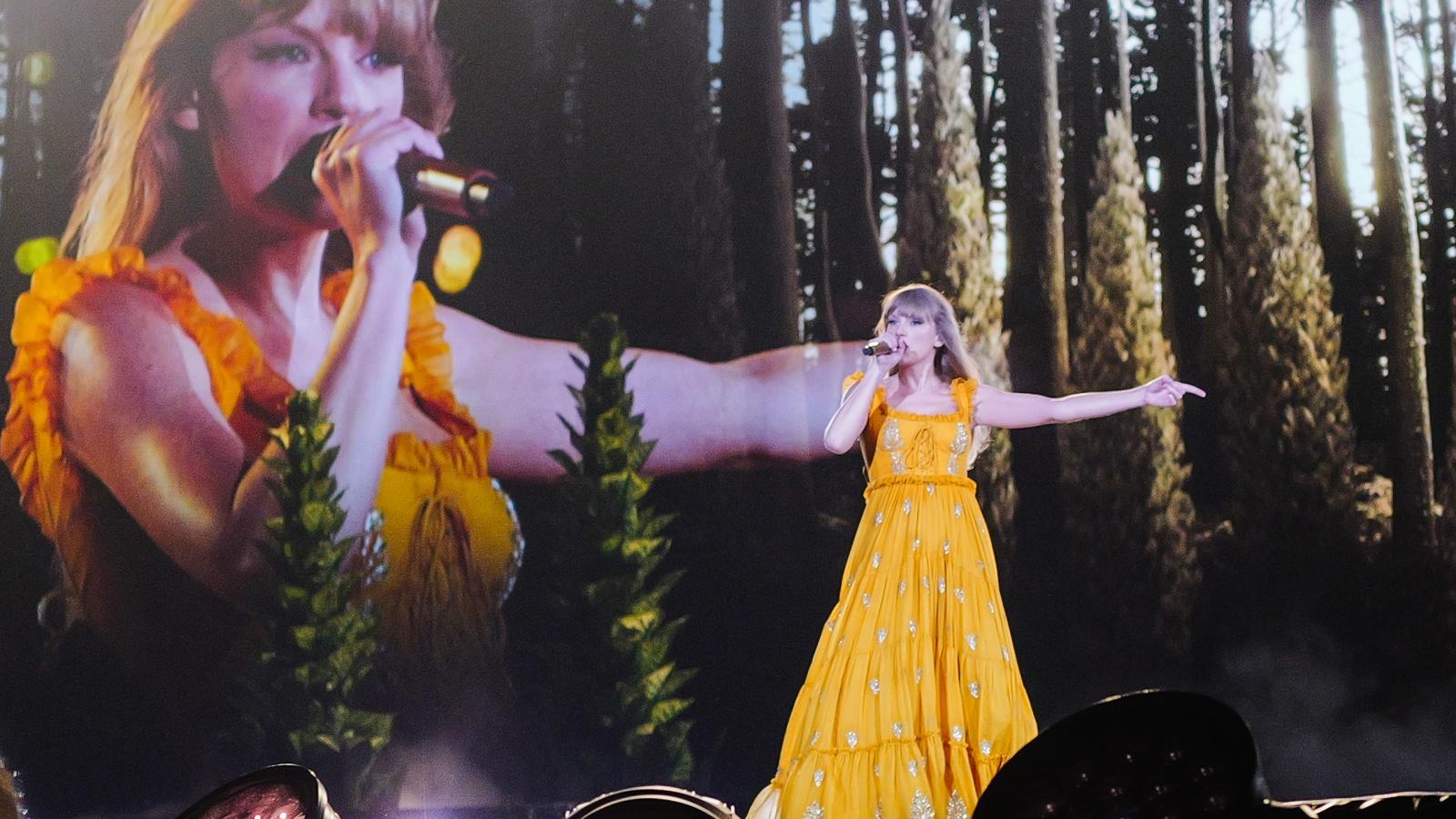 Taylor Swift in a yellow dress performing onstage during her Eras Tour