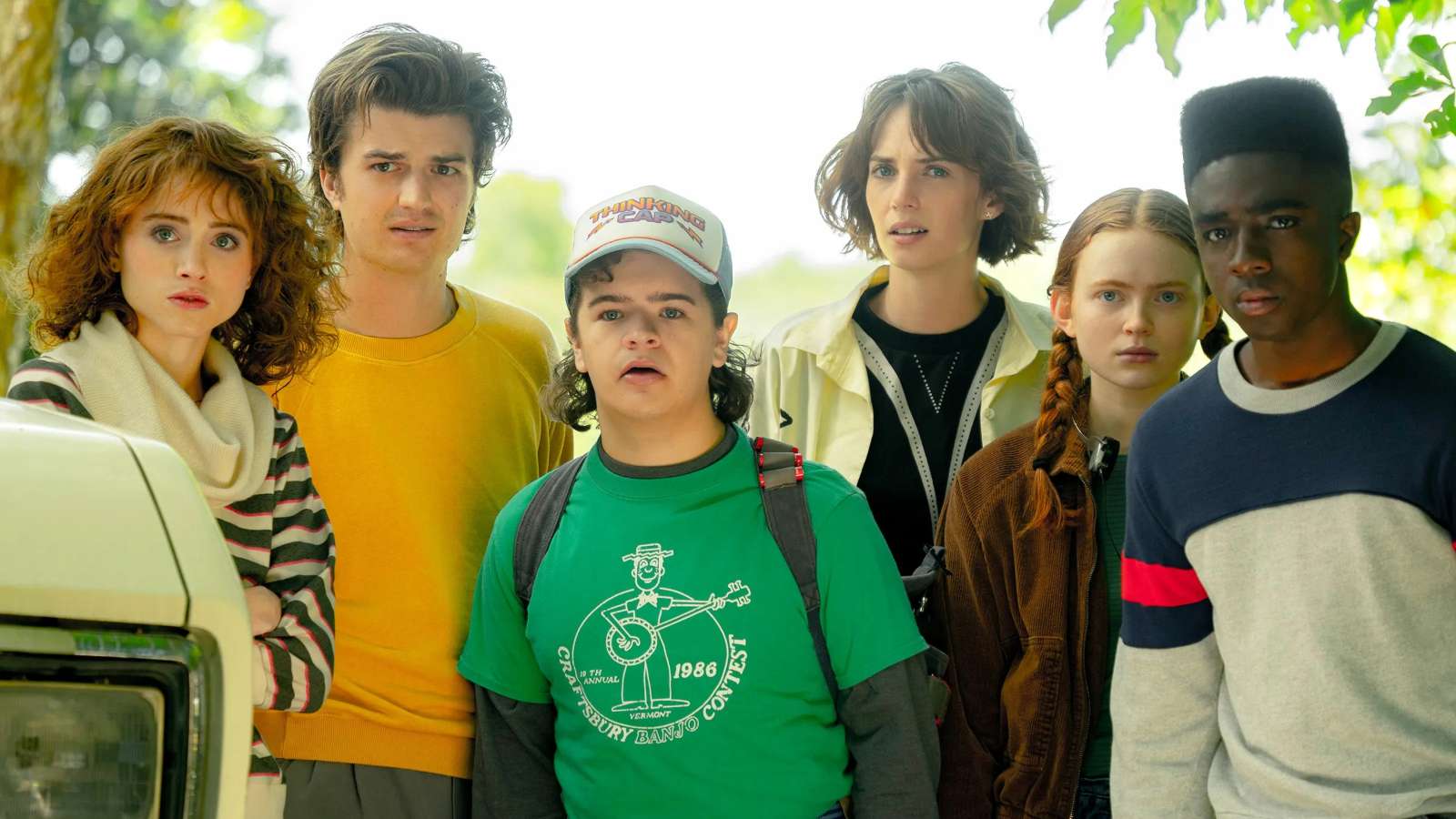 The cast of stranger things standing together outside and looking towards the camera in shock