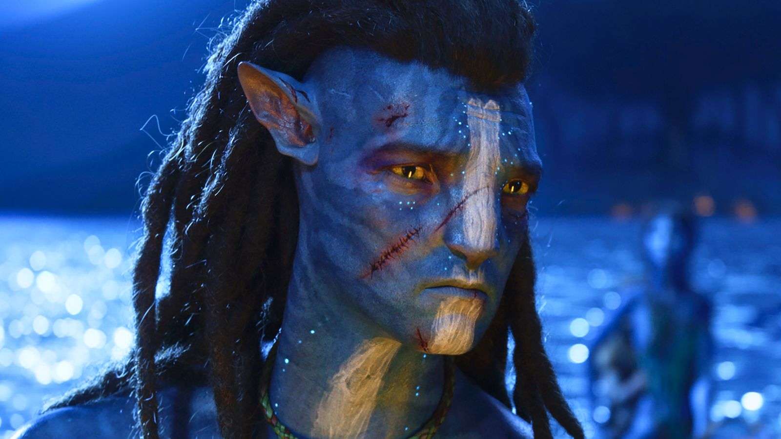 Sam Worthington as Jake Sully in Avatar 2. He stands with water behind him at night.