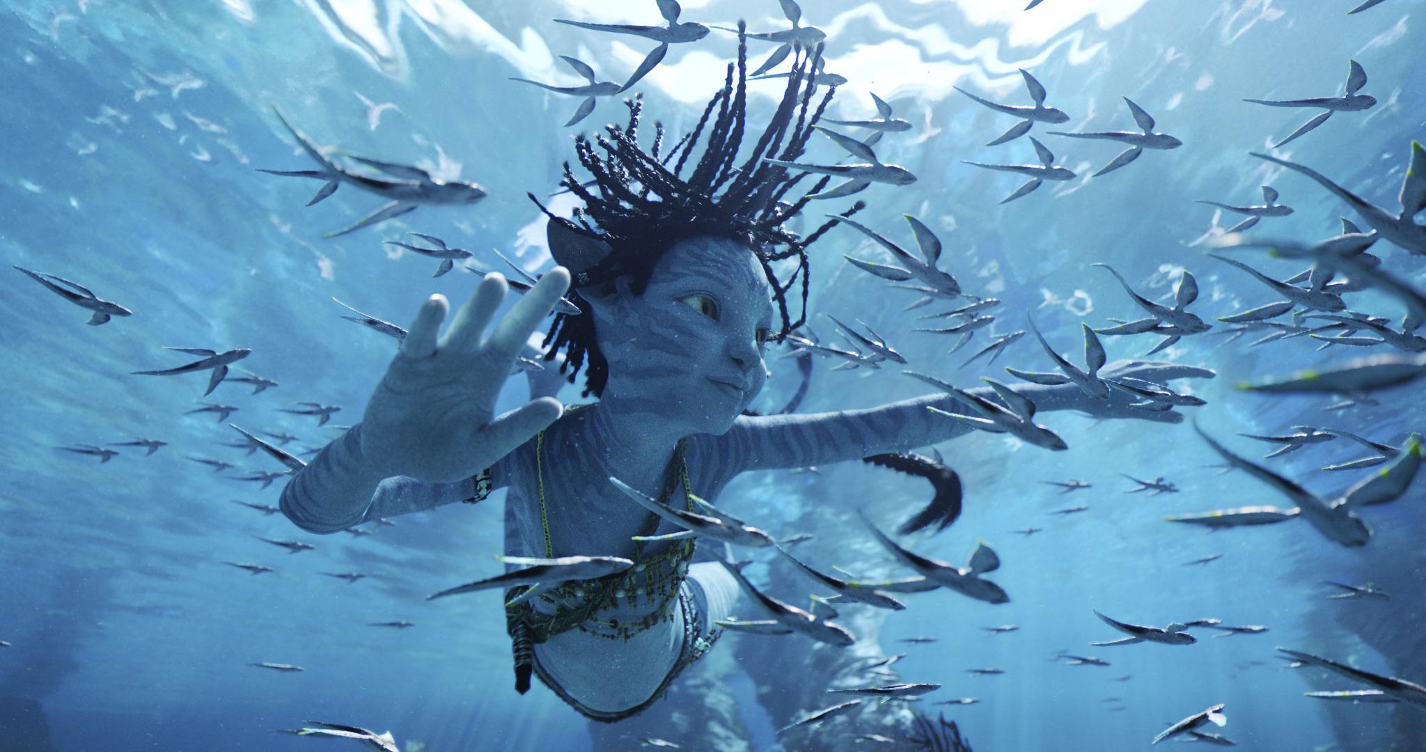 Sigourney Weaver as Kiri in Avatar The Way of Water. She is swimming with fish in the sea.