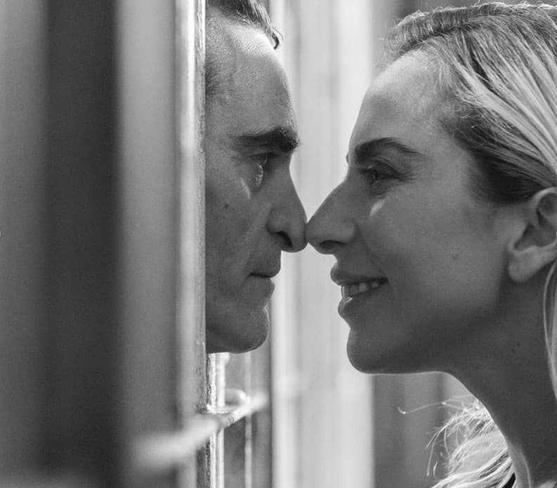 Joaquin Phoenix as Arthur Fleck and Lady Gaga as Harley Quinn in Joker 2. They touch noses through Arthur's prison cell bars.
