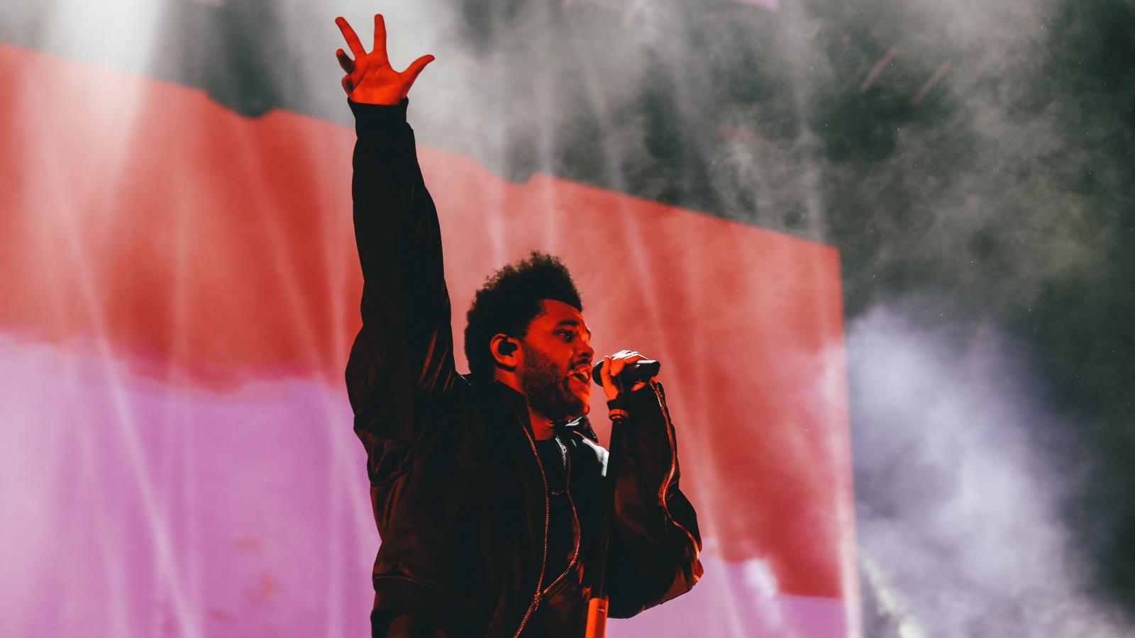 The Weeknd performing onstae with his right hand lifted into the air