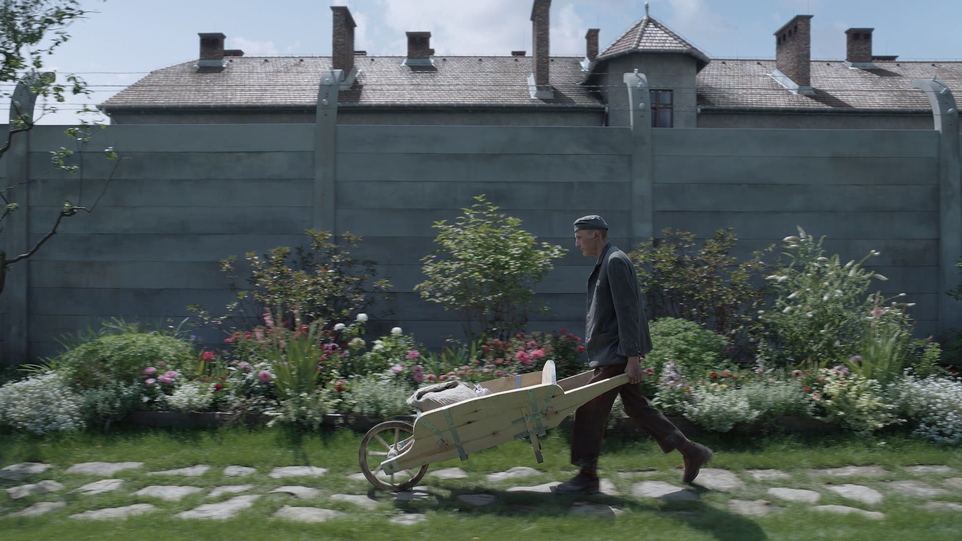 Christian Friedel as Rudolf Höss pushes a wheelbarrow in a garden in The Zone of Interest.