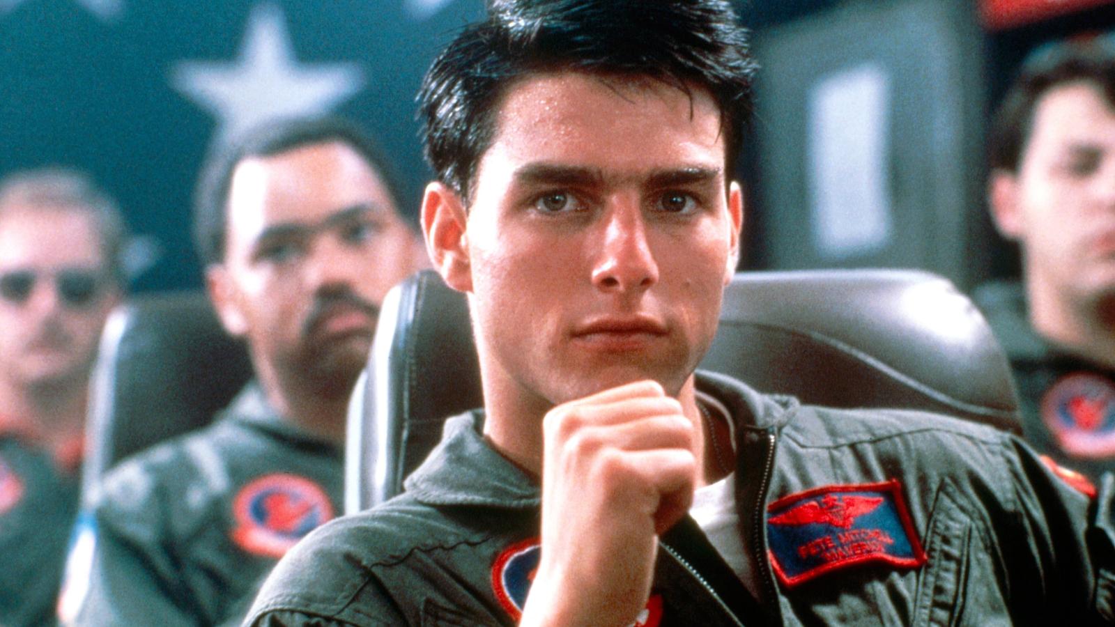 Tom Cruise as Maverick in Top Gun, sitting in a chair with his hand on his chin
