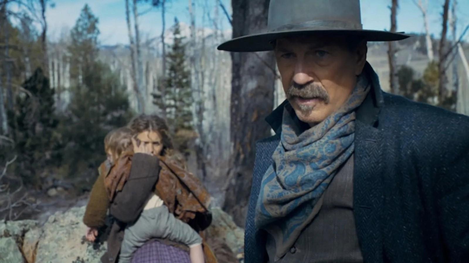 Kevin Costner in the Horizon trailer, standing in the woods with a woman and child behind him