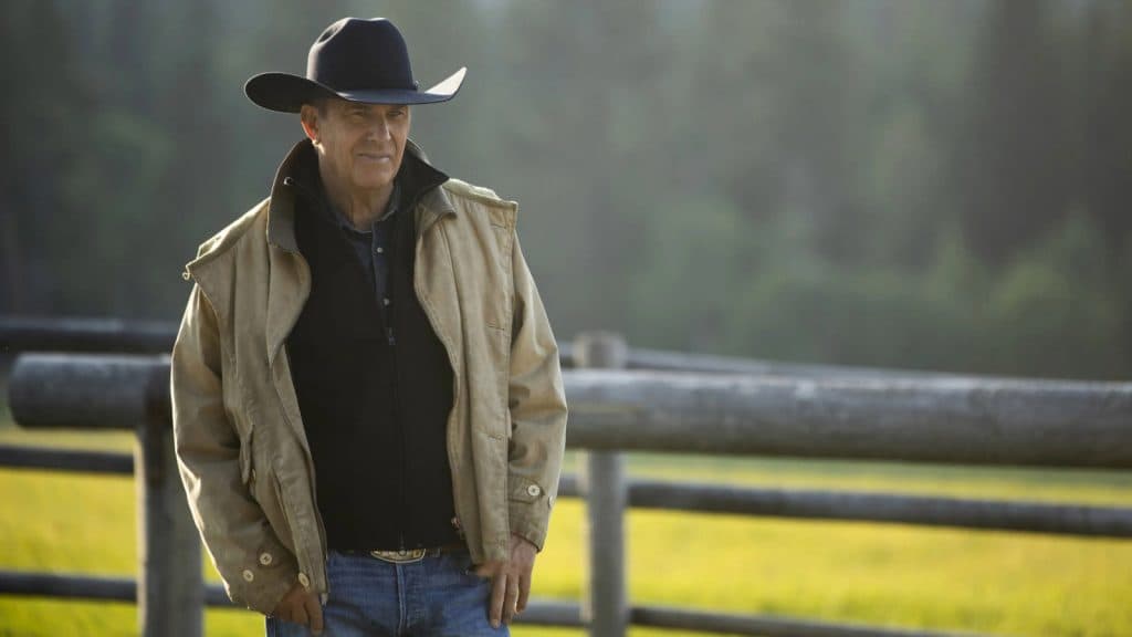 Kevin Costner as John Dutton in Yellowstone, wearing a cowboy hat and standing in a field