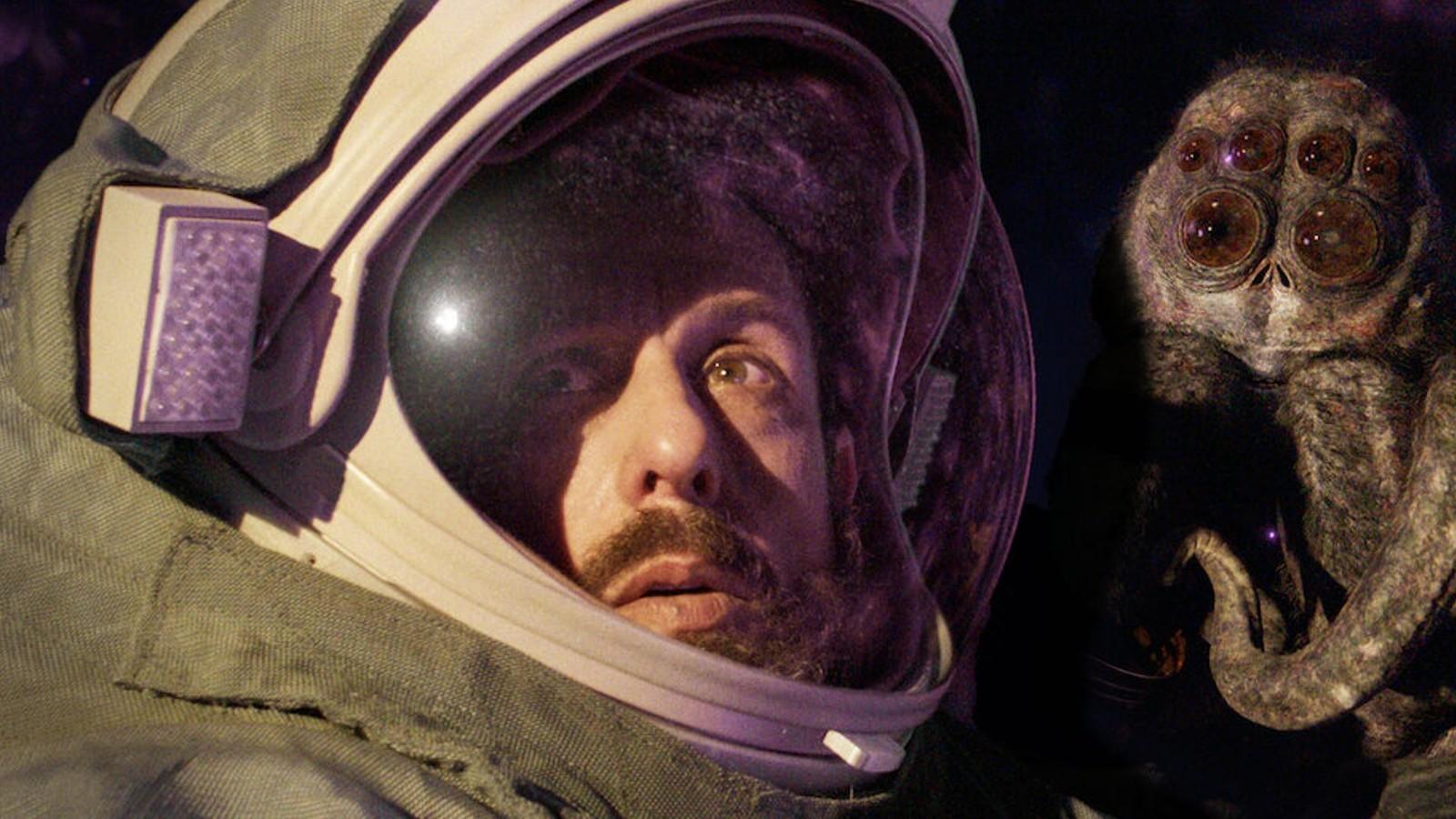 Adam Sandler in Spaceman stands in a spacesuit with a huge spider behind him.
