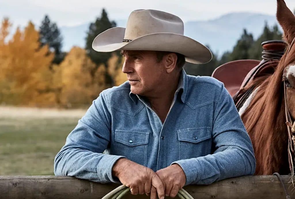 Kevin Costner as John Dutton in Yellowstone: standing next to a horse and leaning against a fence
