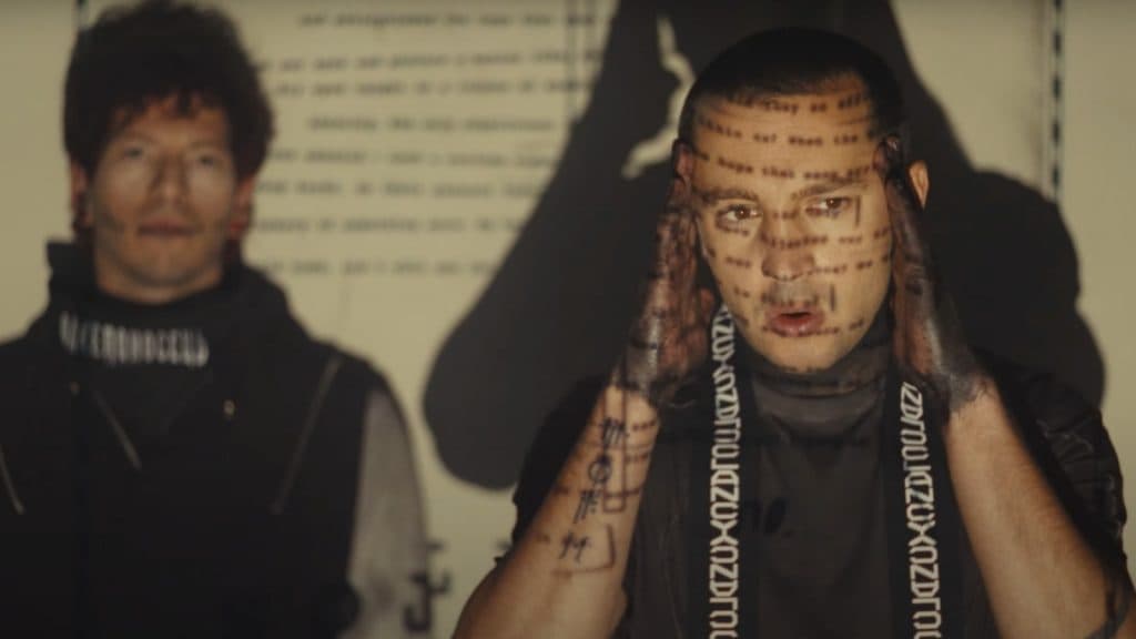 Twenty One Pilots stand in front of a projection machine in 'Overcompensate' video