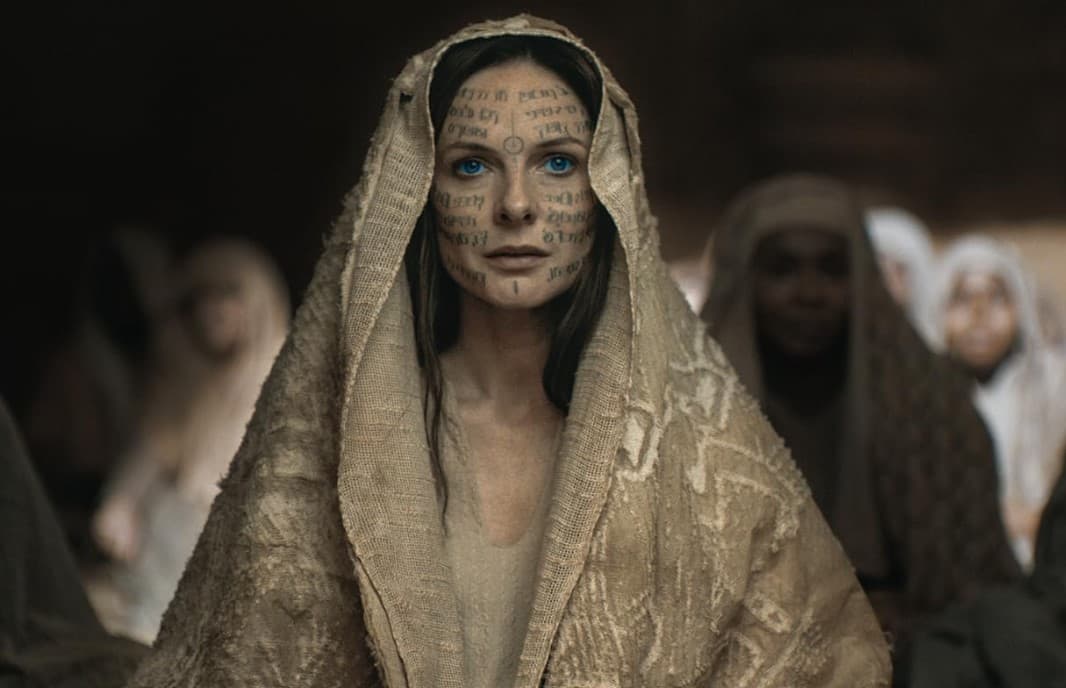 Rebecca Ferguson as Lady Jessica in Dune 2. She has Fremen scripture written on her face and wears a beige cloak.