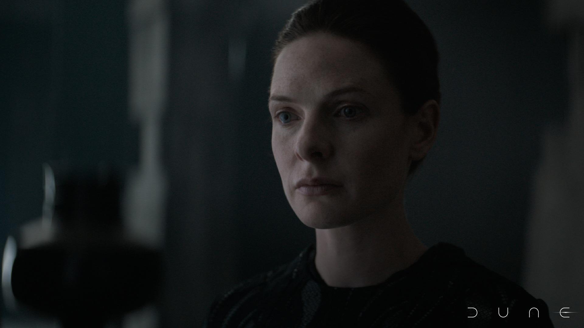 Rebecca Ferguson as Lady Jessica in Dune. She is in a dark room, with half of her face covered by shadow.