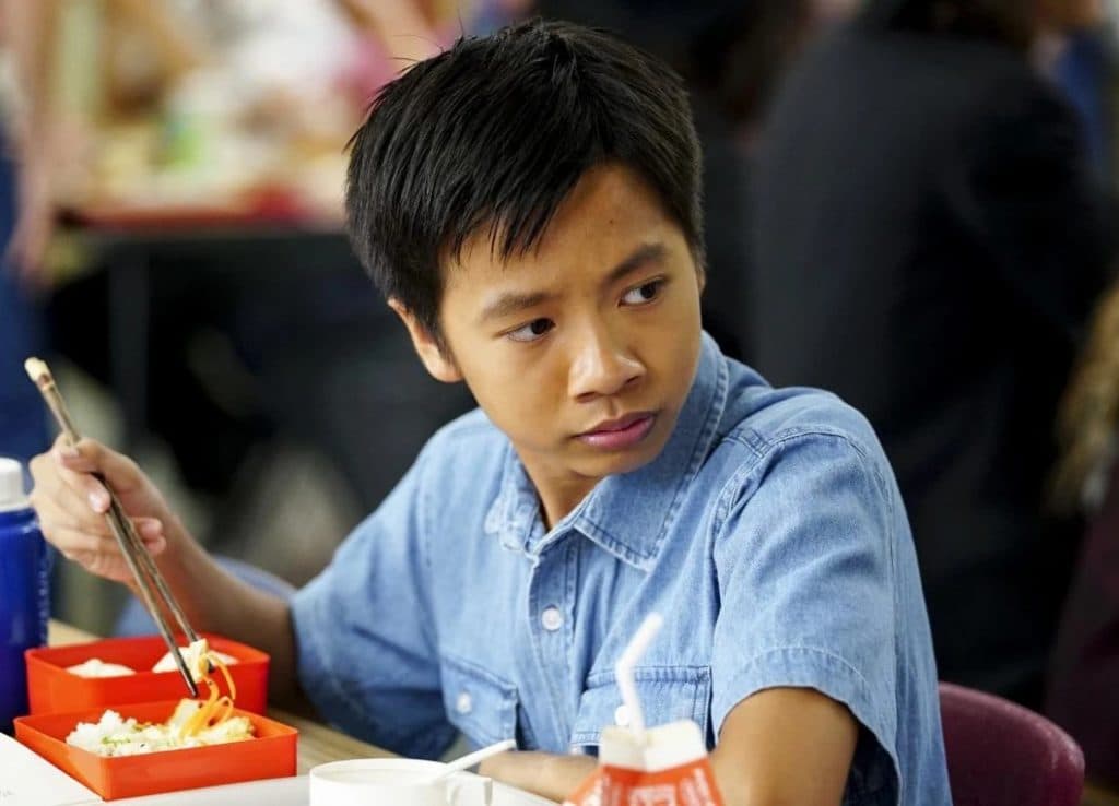 Ryan Phuong as Tam in Young Sheldon, sitting at a table eating lunch