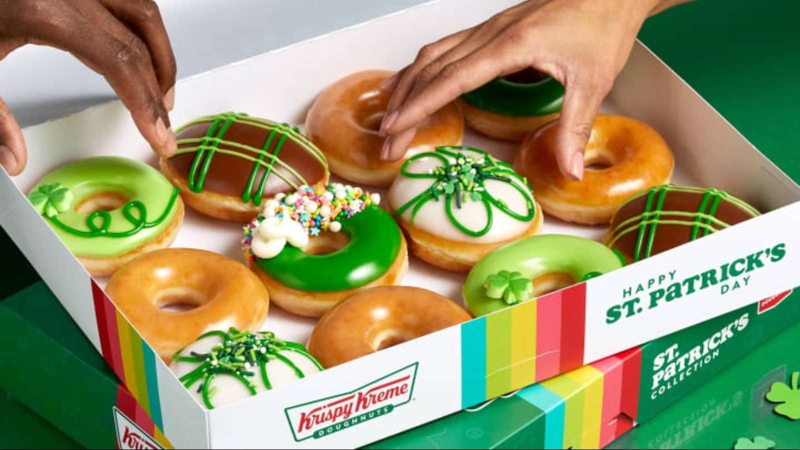 A photo of two people's hands reaching for donut's from a box of twelve donuts