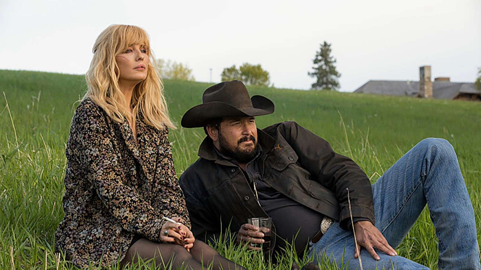 Kelly Reilly and Cole Hauser as Beth and Rip in Yellowstone, laying on the grass