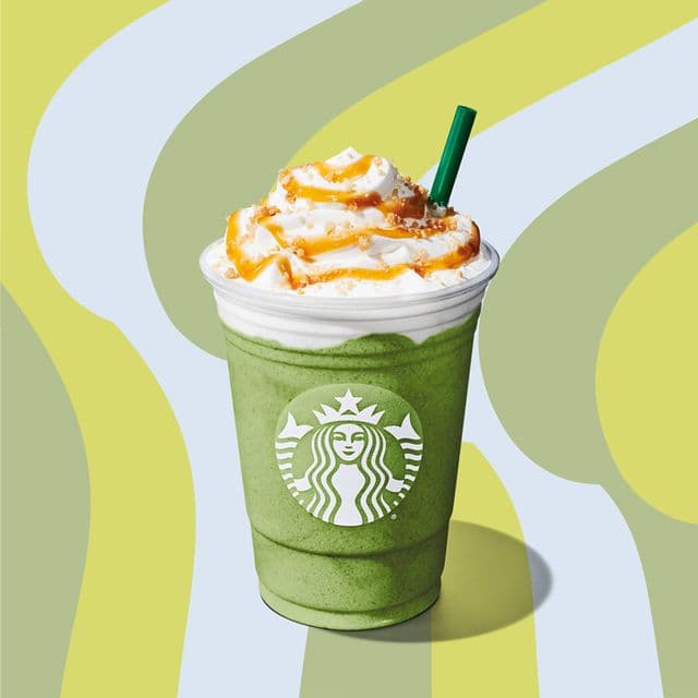 A green Starbucks drink with whipped cream and straw on a green swirl background.