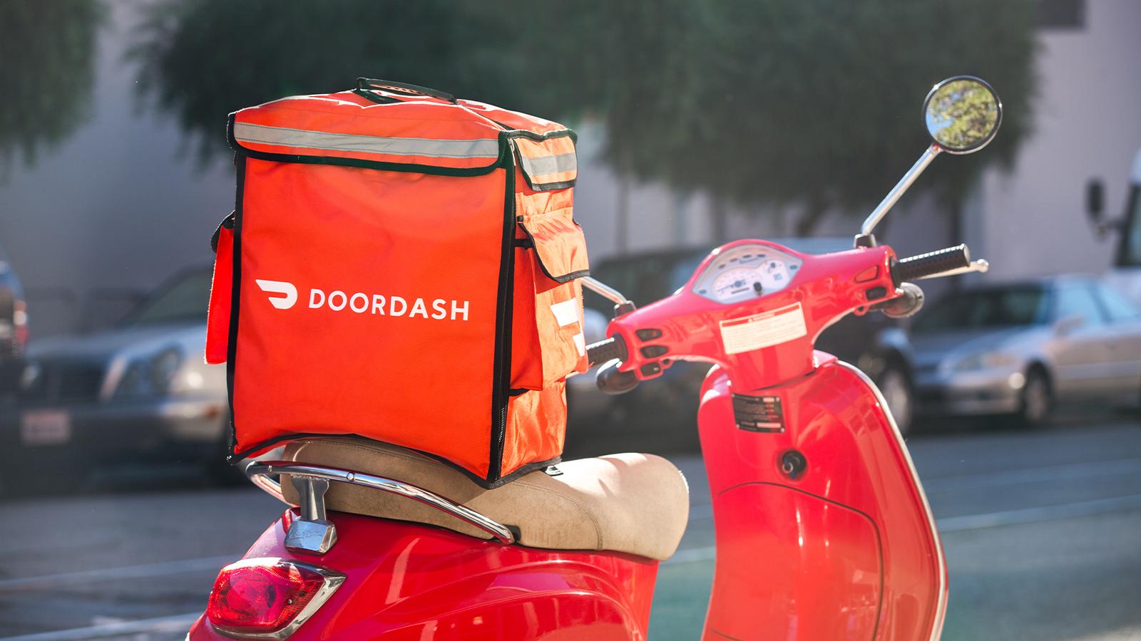 A red scooter with a DoorDash bag on the seat