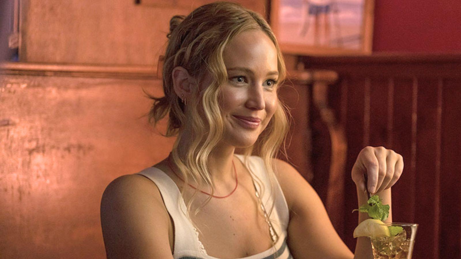 Jennifer Lawrence in No Hard Feelings. She sits at a table in a bar stirring her drink.