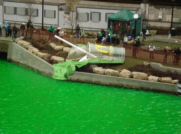 A giant shamrock shake sculpture spilling into a river dyed green.