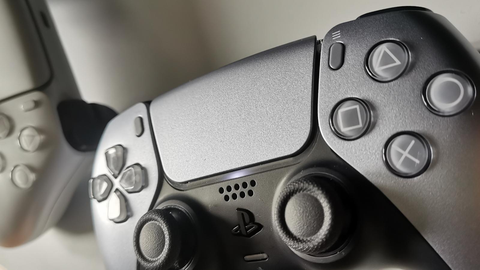 Photo of a DualSense controller sitting on a PS5, with another DualSense on the left-hand side.