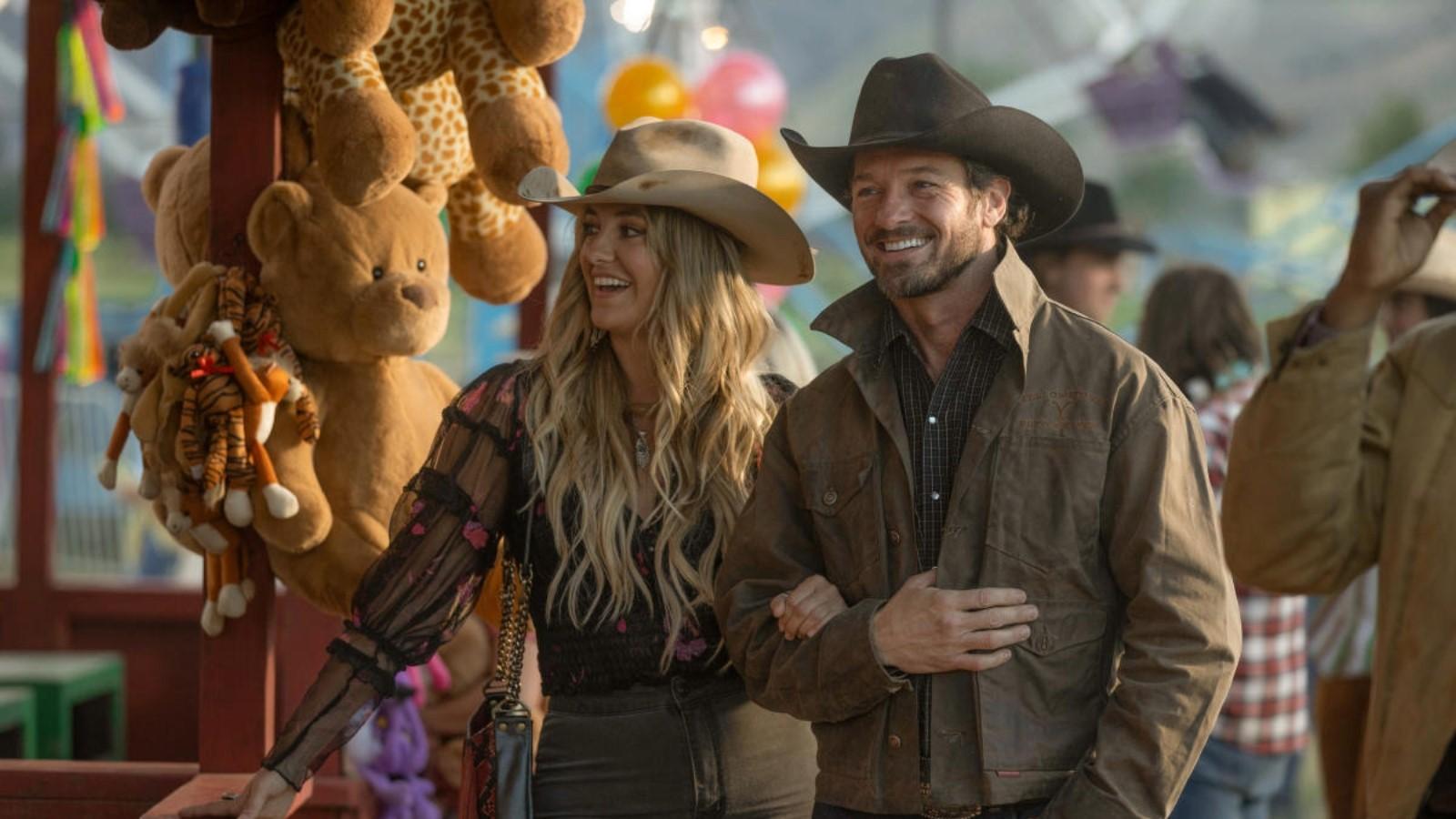 Lainey Wilson as Abby and Ian Bohen as Ryan in Yellowstone, walking through a carnival and holding arms