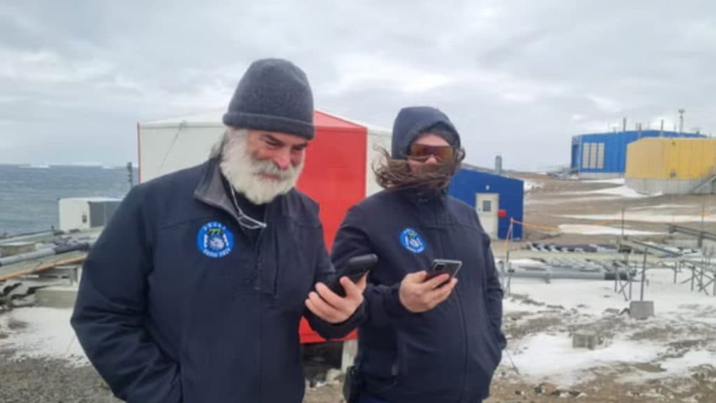 Two scientists stood in Antarctica hold their phones aloft, with Pokemon Go visible on the screens