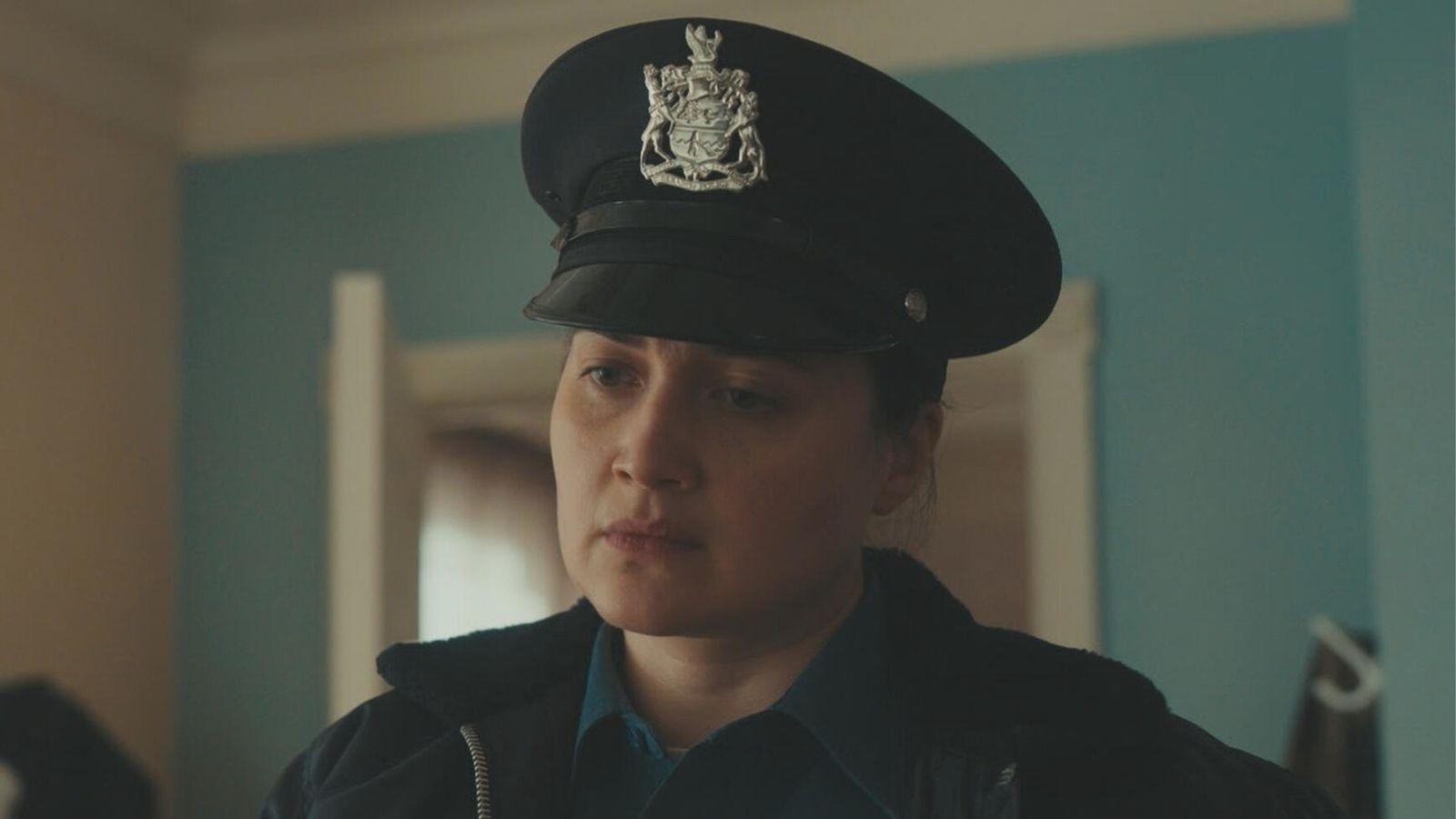 Lily Gladstone in Under the Bridge stands in a home in her police uniform.