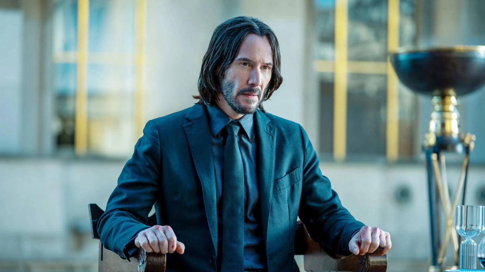 Keanu Reeves as John Wick in John Wick 4, sitting in a chair and wearing a suit