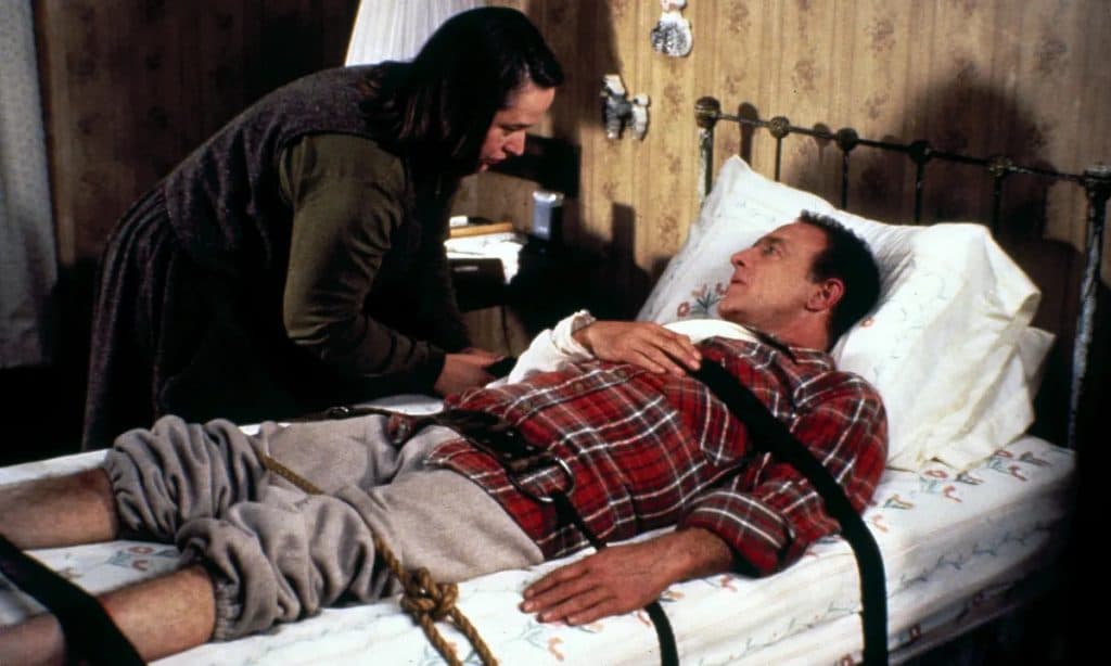 Kathy Bates as Annie Wilkes in Misery, swinging a hammer onto Paul in a bed