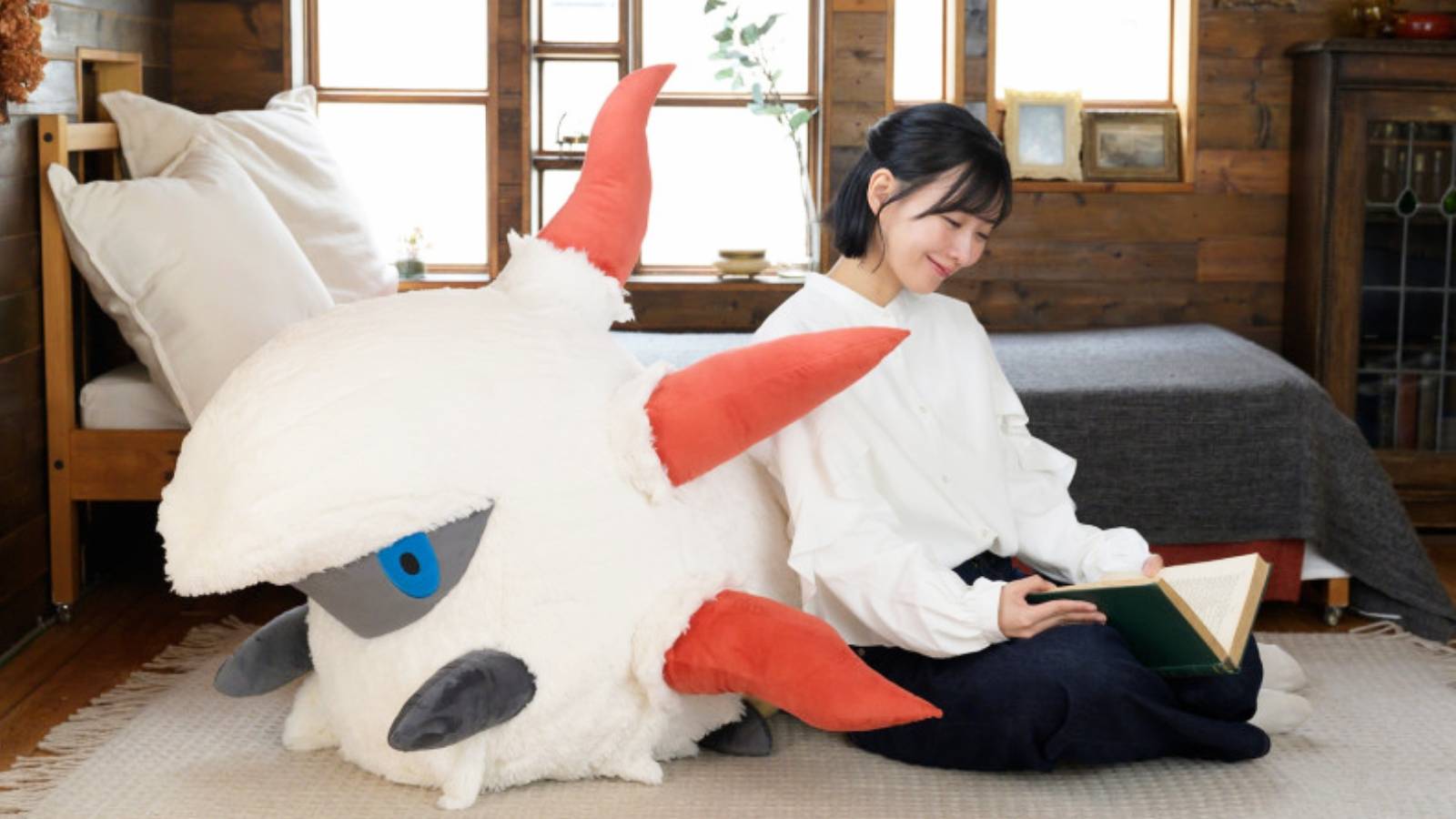 A promotional image for a life size Larvesta plush shows the large stuffed toy next to a person reading